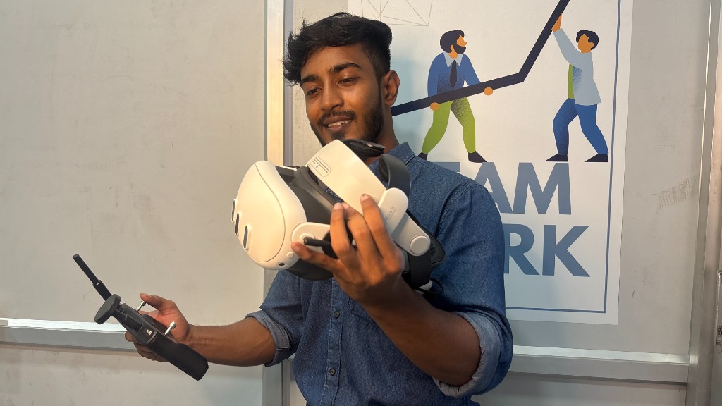 Student holding a VR headset and drone remote controller in the training lab